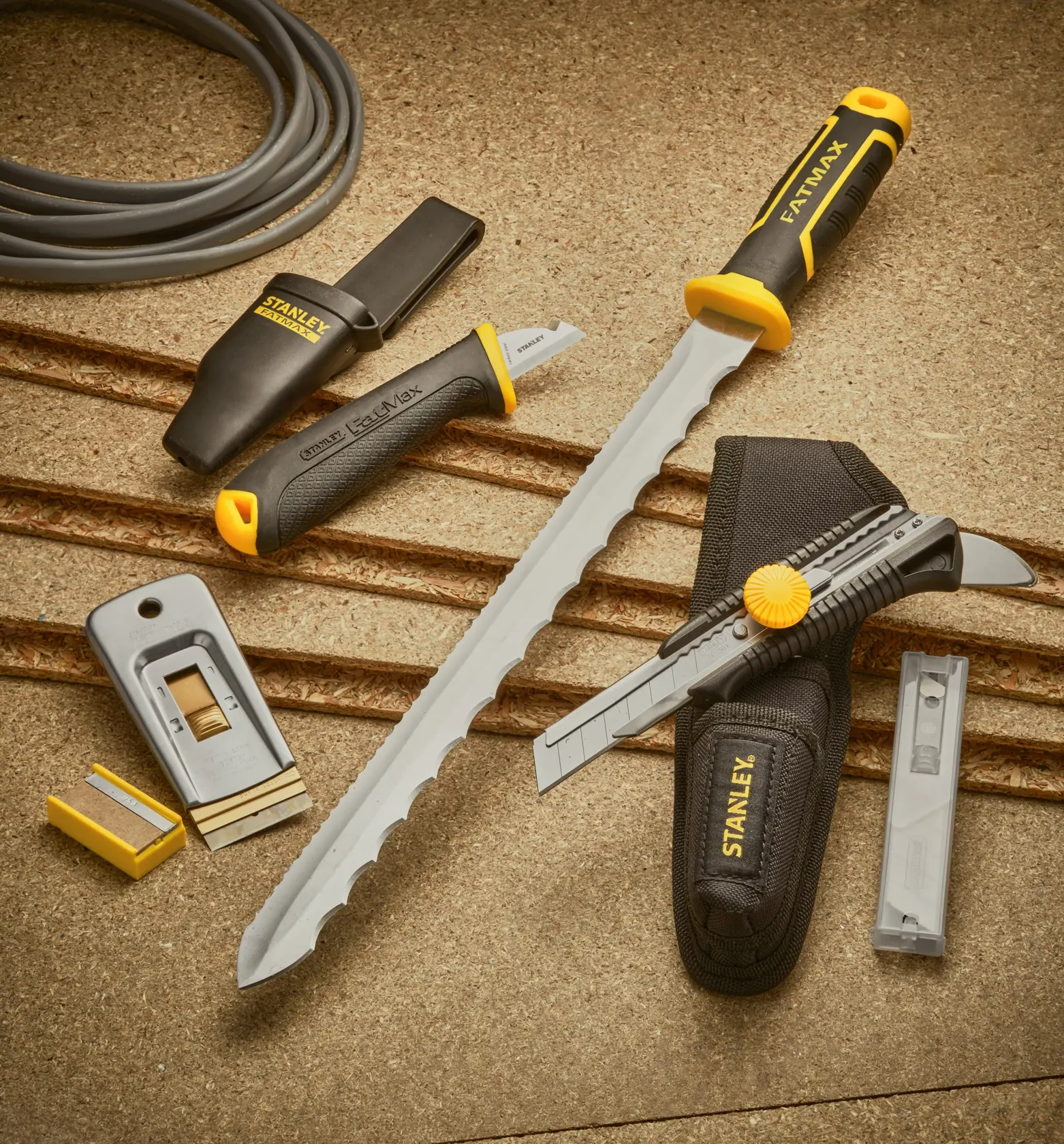 STANLEY 0-28-500 set of hand tools with cutting knives, a rasp, utility blades, and black-yellow handles on a tan surface.