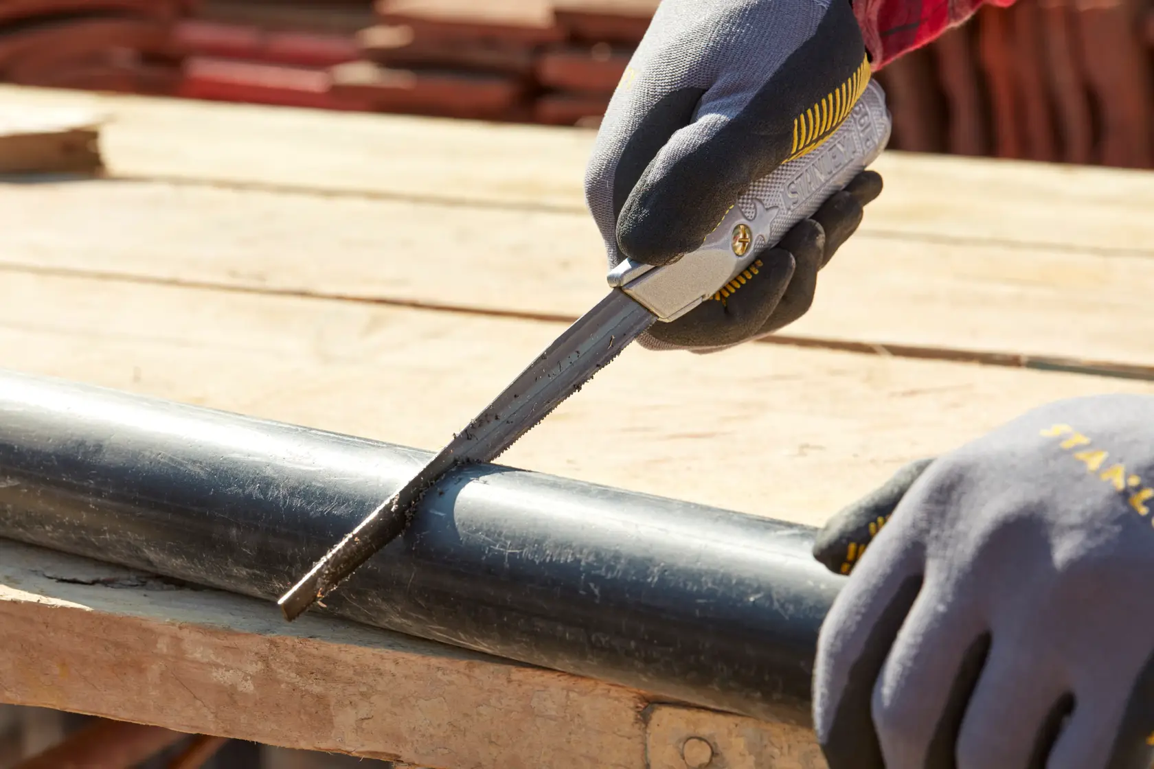 Photo of STANLEY 0-10-129 utility knife cutting a black plastic pipe, worker with gloves in outdoor setting.