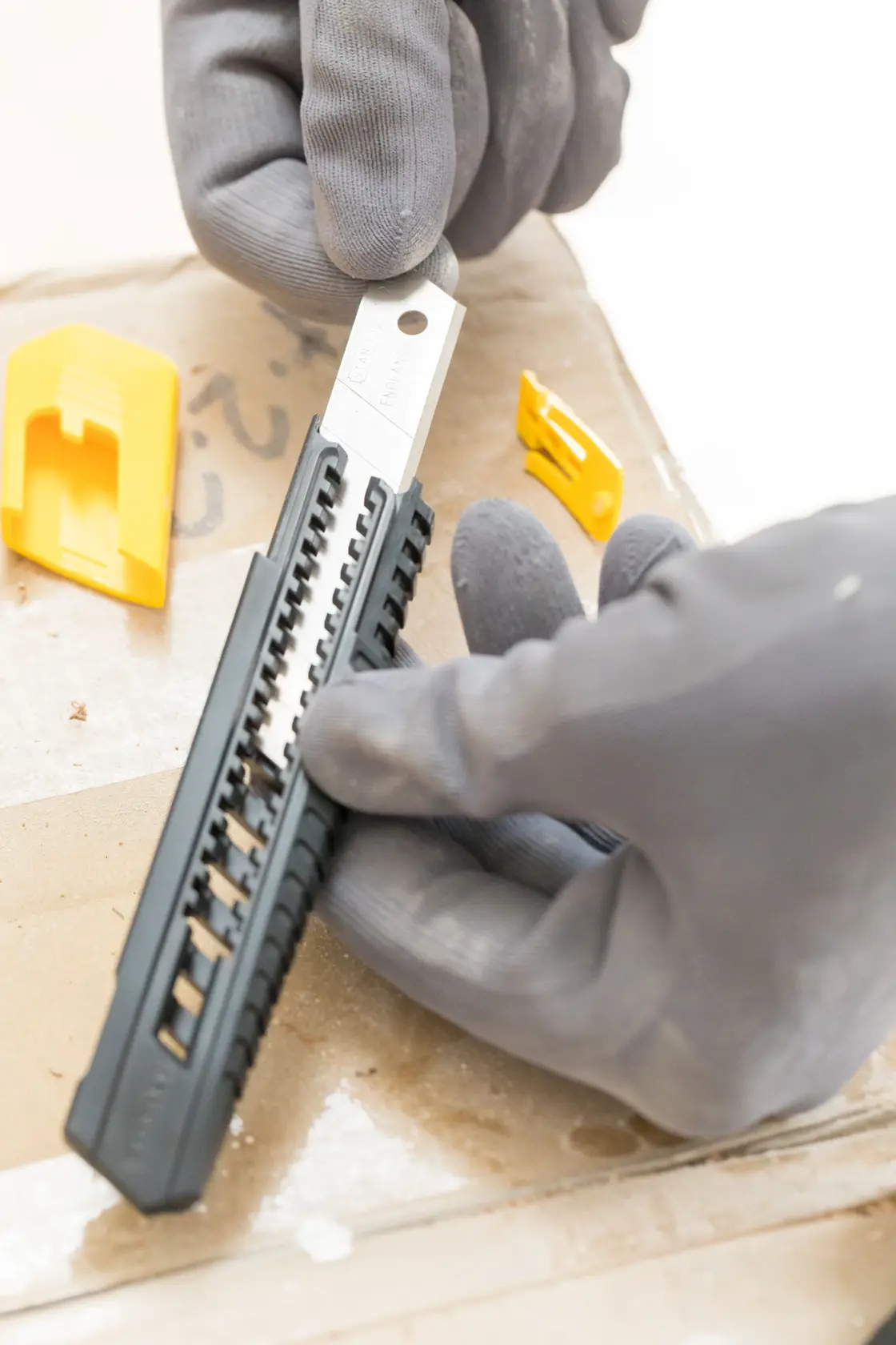 Photo of STANLEY 0-10-151 snap-off knife with black handle and gray blade, held by gloved hands, with yellow covers nearby.