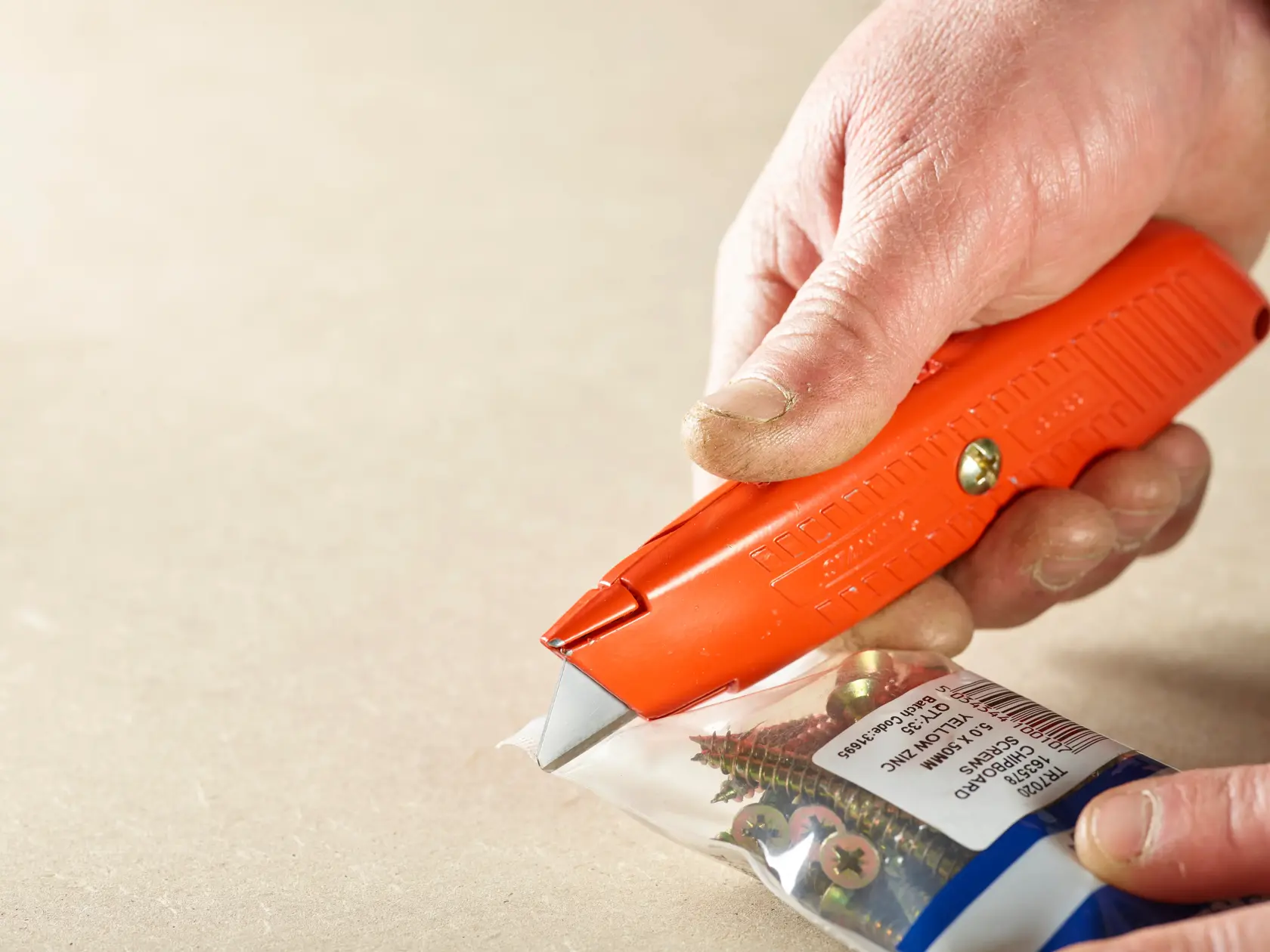 STANLEY 0-10-189 orange utility knife cutting a plastic bag of screws, close-up photography.
