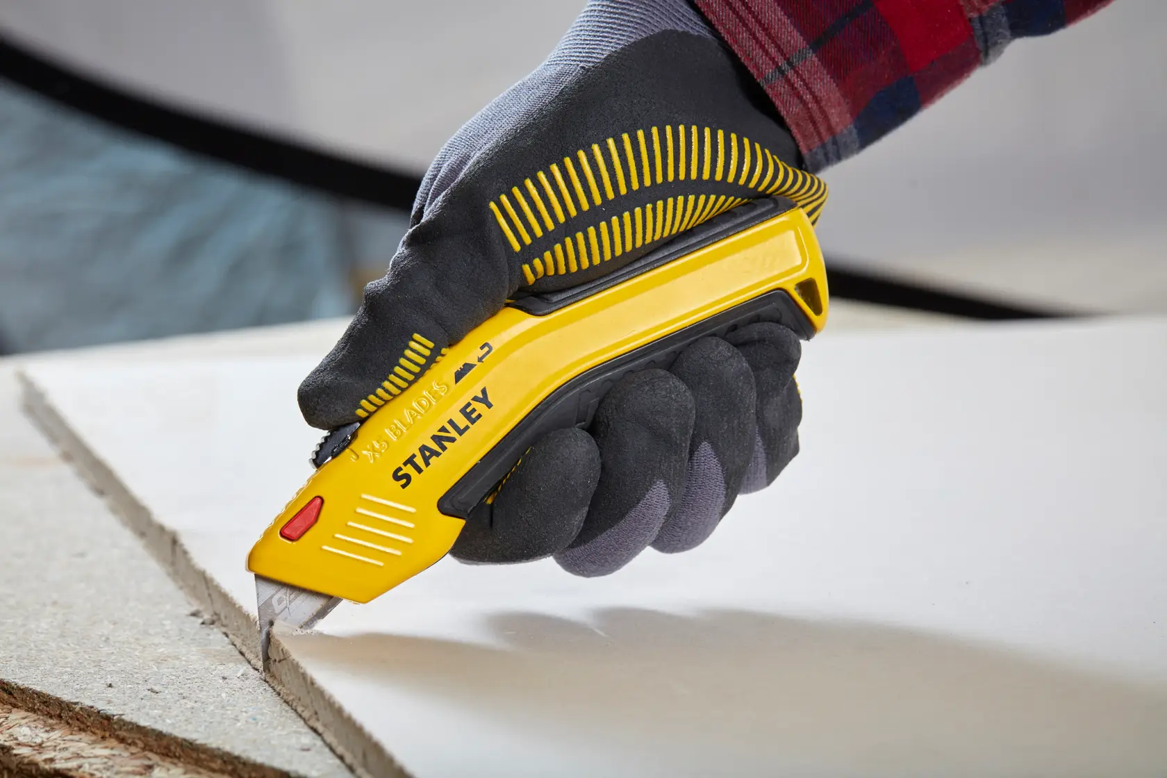 STANLEY 0-10-237 utility knife cutting drywall, close-up, held by gloved hand.