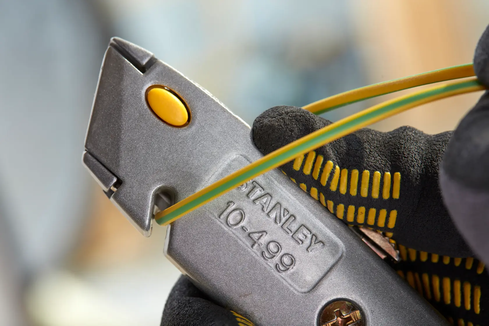 STANLEY 0-10-499 utility knife silver body with yellow button in gloved hand, close-up side angle.