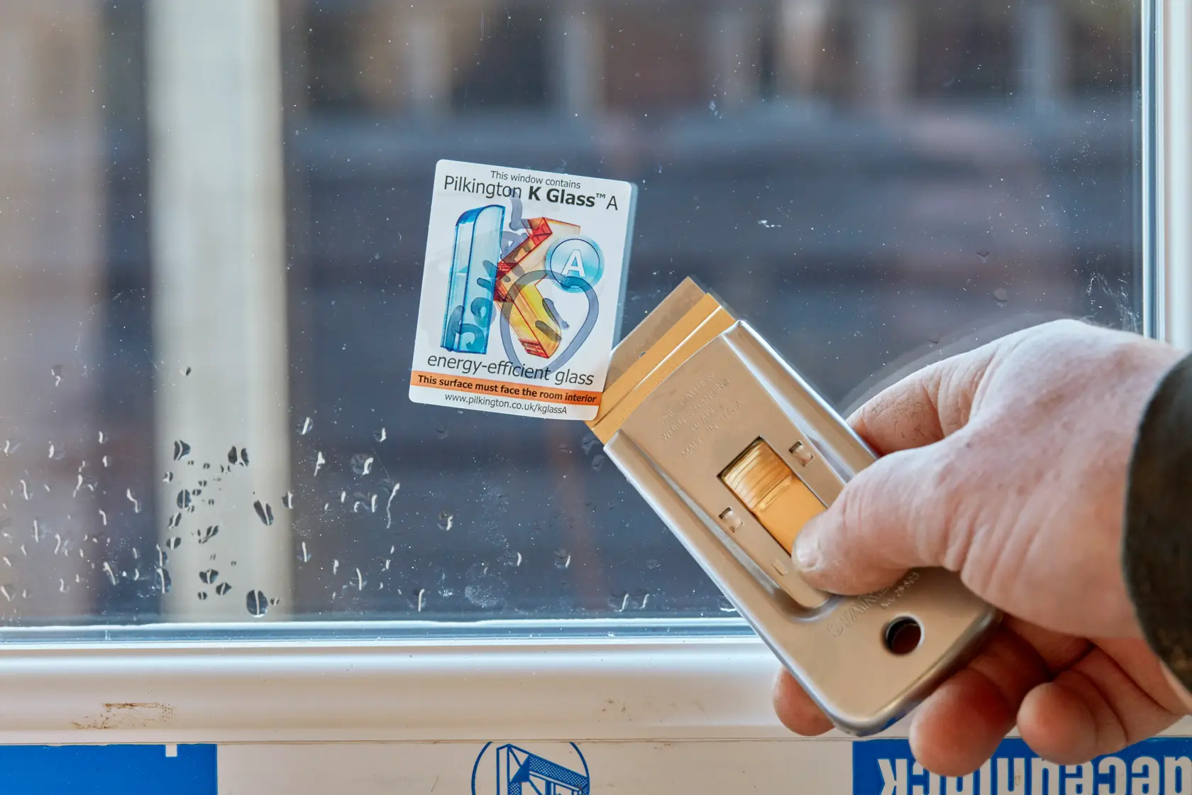 STANLEY 0-28-500 retractable window scraper removing sticker from glass, close-up.