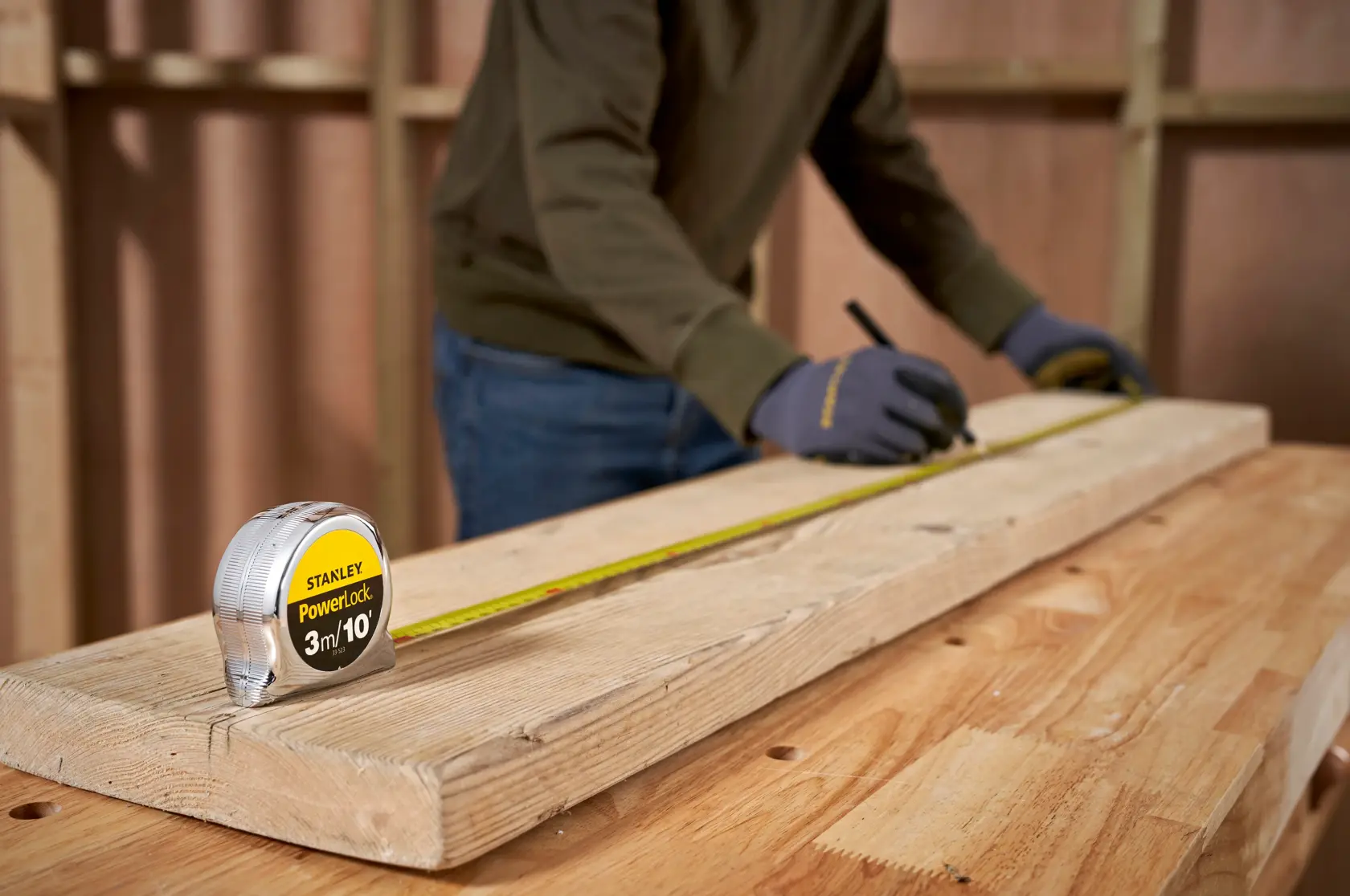 STANLEY 0-33-523 tape measure on wood plank, person marking measurements in workshop setting.