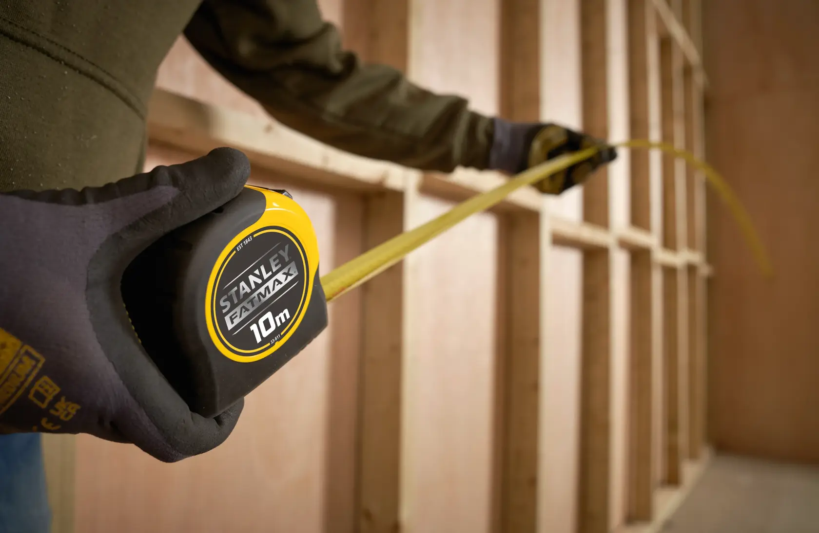 Photo of STANLEY 0-33-811 tape measure being used for measuring wooden framing, close-up of gloved hand holding the tool.