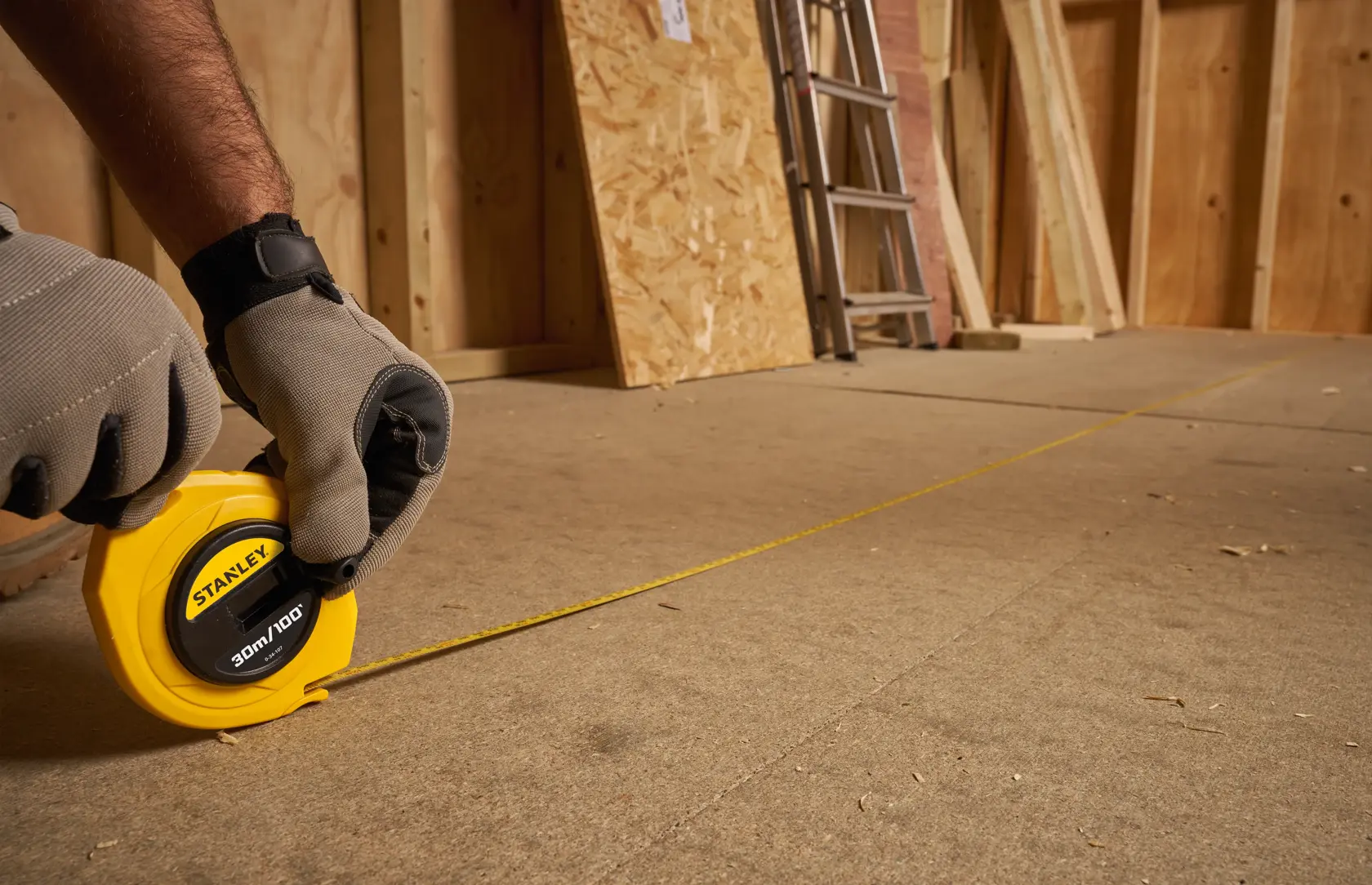 STANLEY 0-34-107 measuring tape in use on construction floor, gloves holding yellow case.