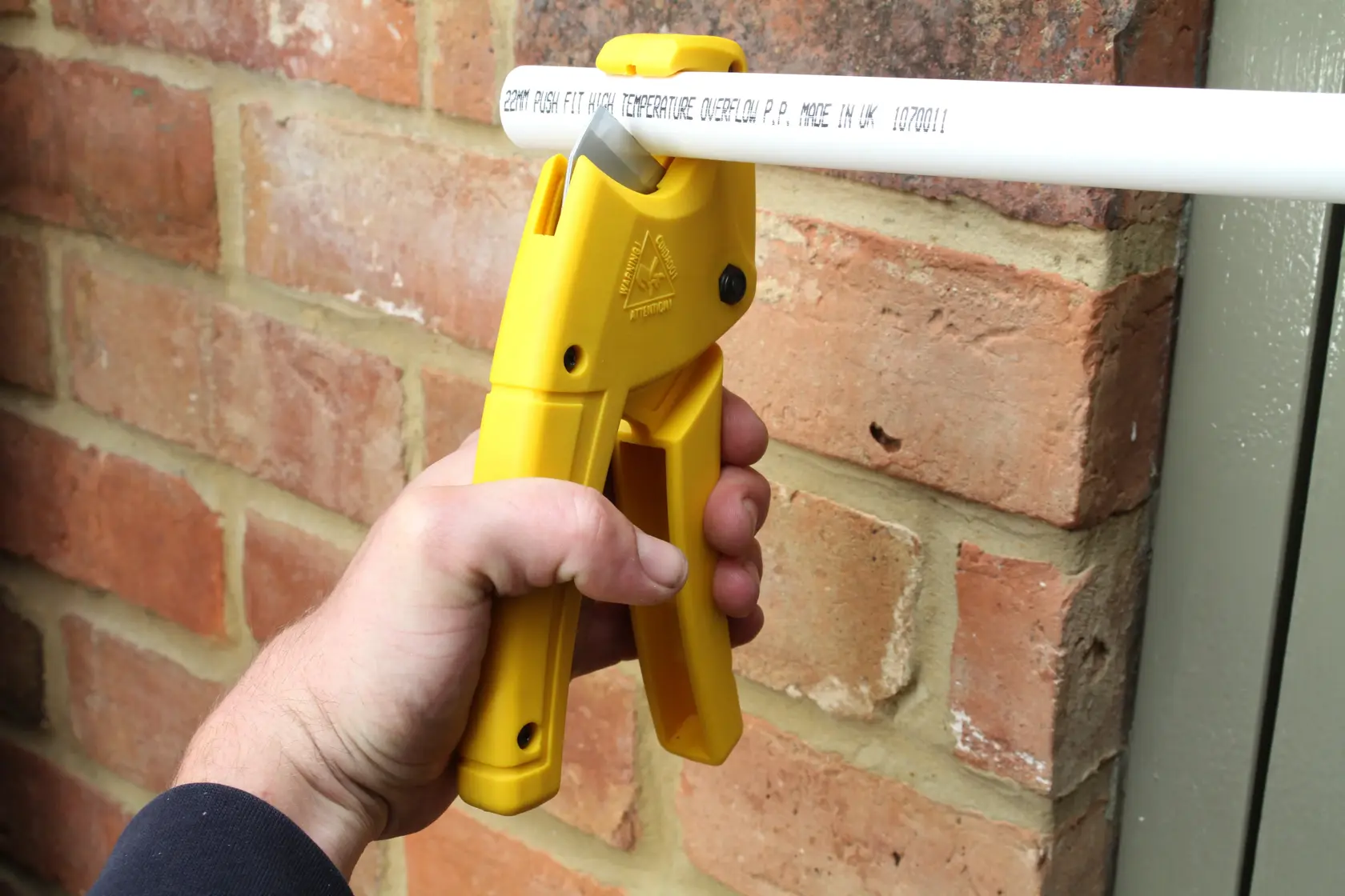 STANLEY 0-70-450 pipe cutter in yellow used to cut a white pipe near a brick wall, close-up photography.
