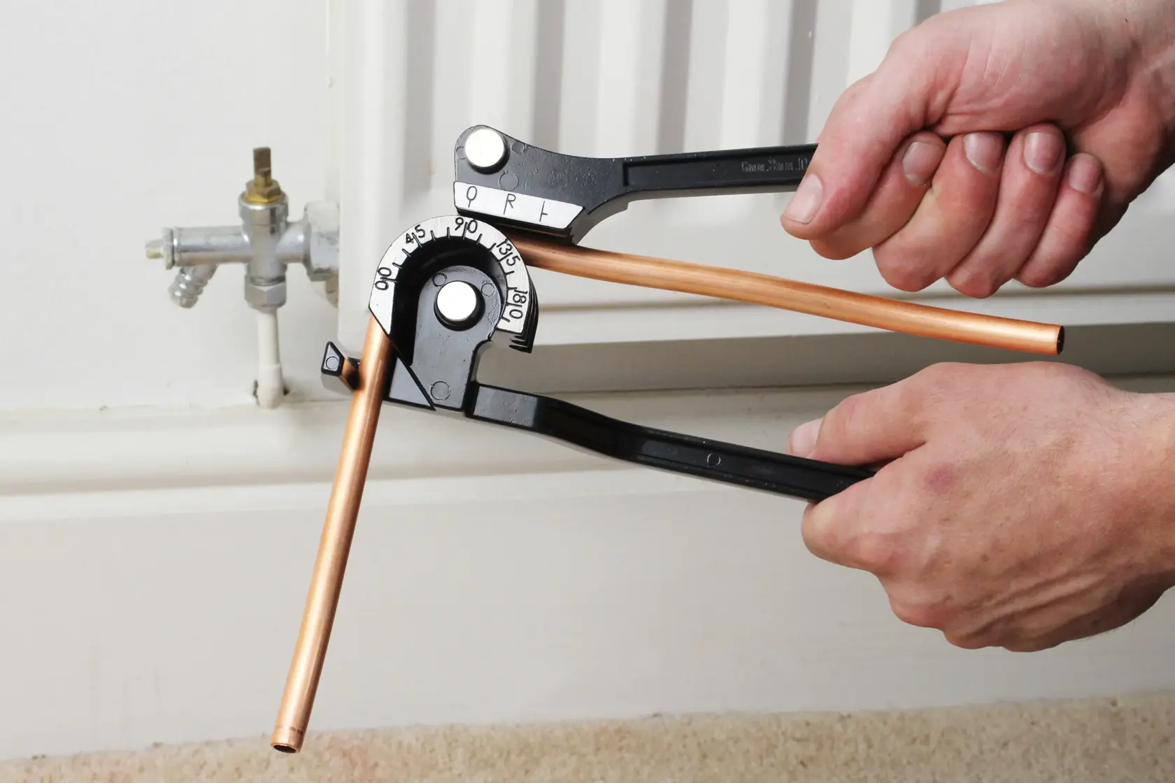 Photo of STANLEY 0-70-451 pipe bender in use, bending a copper pipe near a radiator pipe fitting.