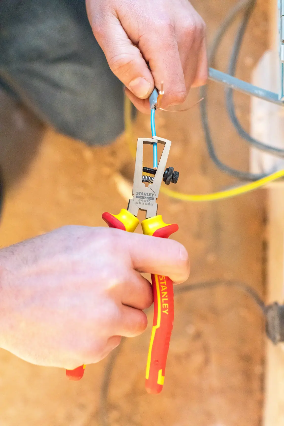 STANLEY 0-84-010 wire stripper with red/yellow handle stripping blue wire during installation.