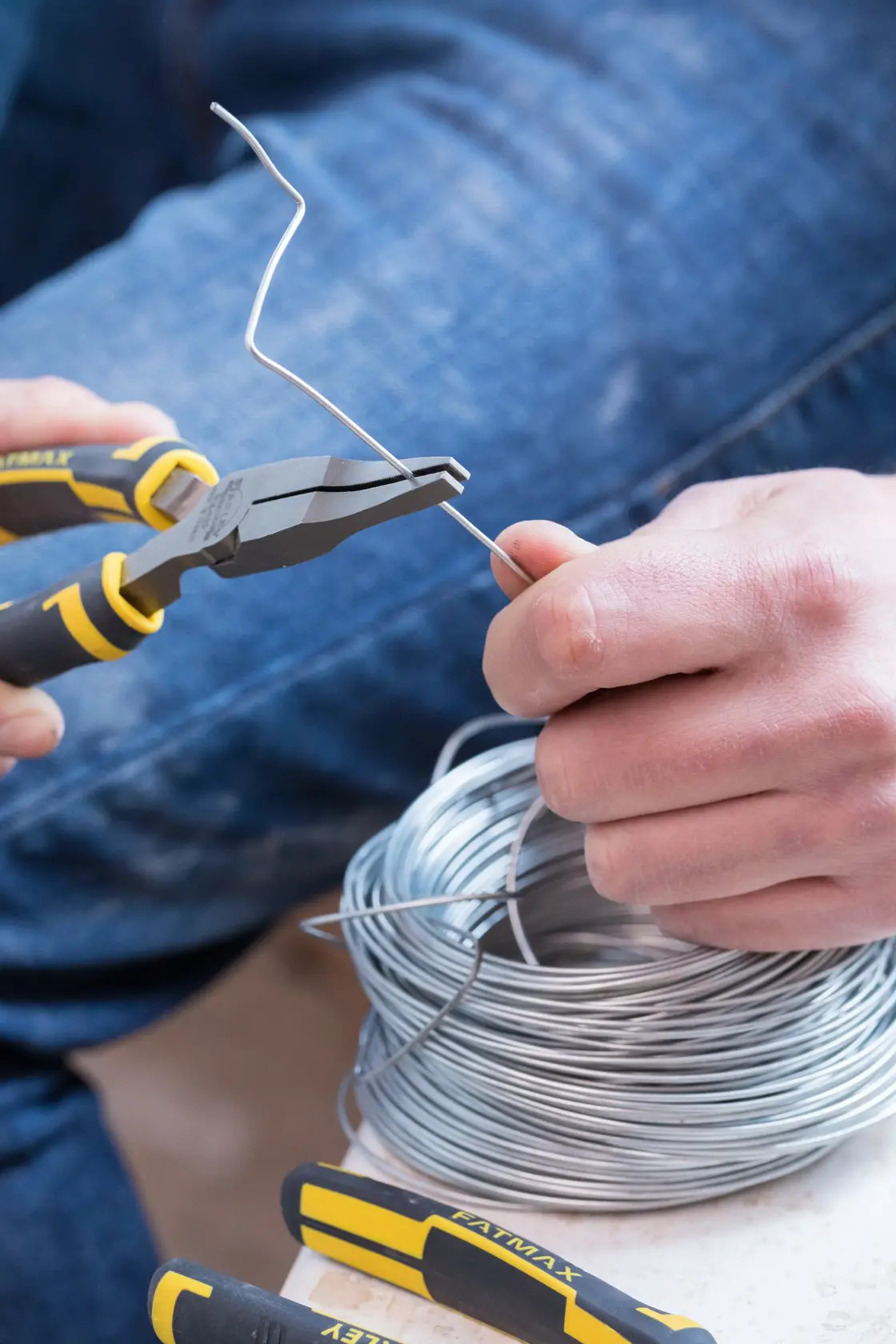 STANLEY 0-84-495 pliers in use, cutting silver wire, close-up, with coil and jeans visible.