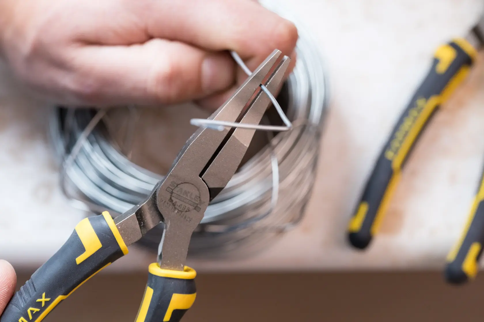 STANLEY 0-84-495 pliers with black and yellow handle, gripping metal wire close-up.