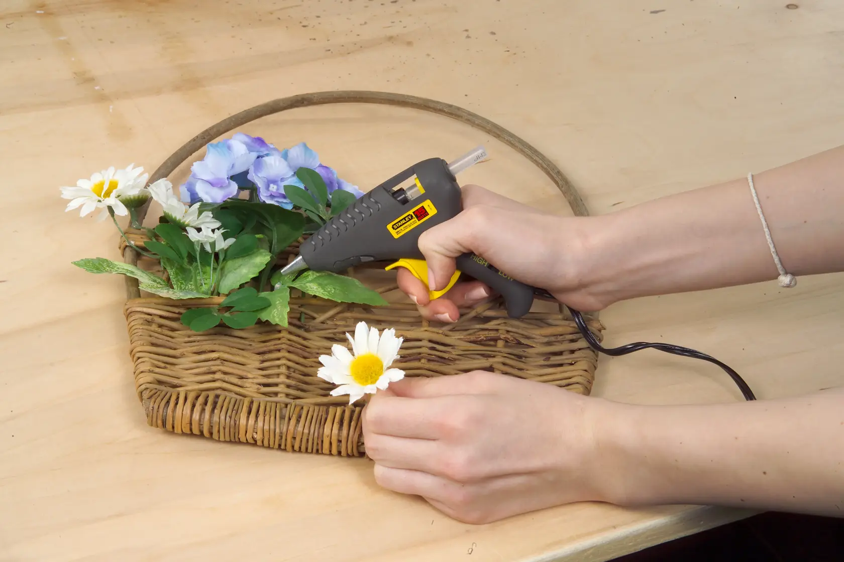 STANLEY 0-GR15 glue gun used to attach flowers to a wicker basket on a wooden table, front angle.
