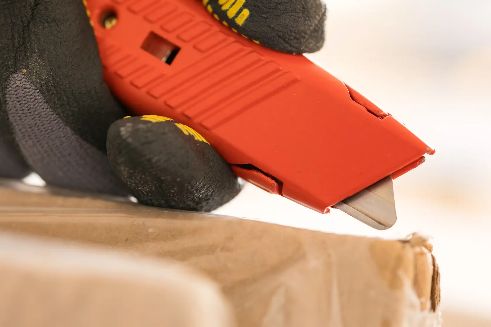 STANLEY 1-10-189 red utility knife close-up cutting cardboard, gloved hand holding tool.