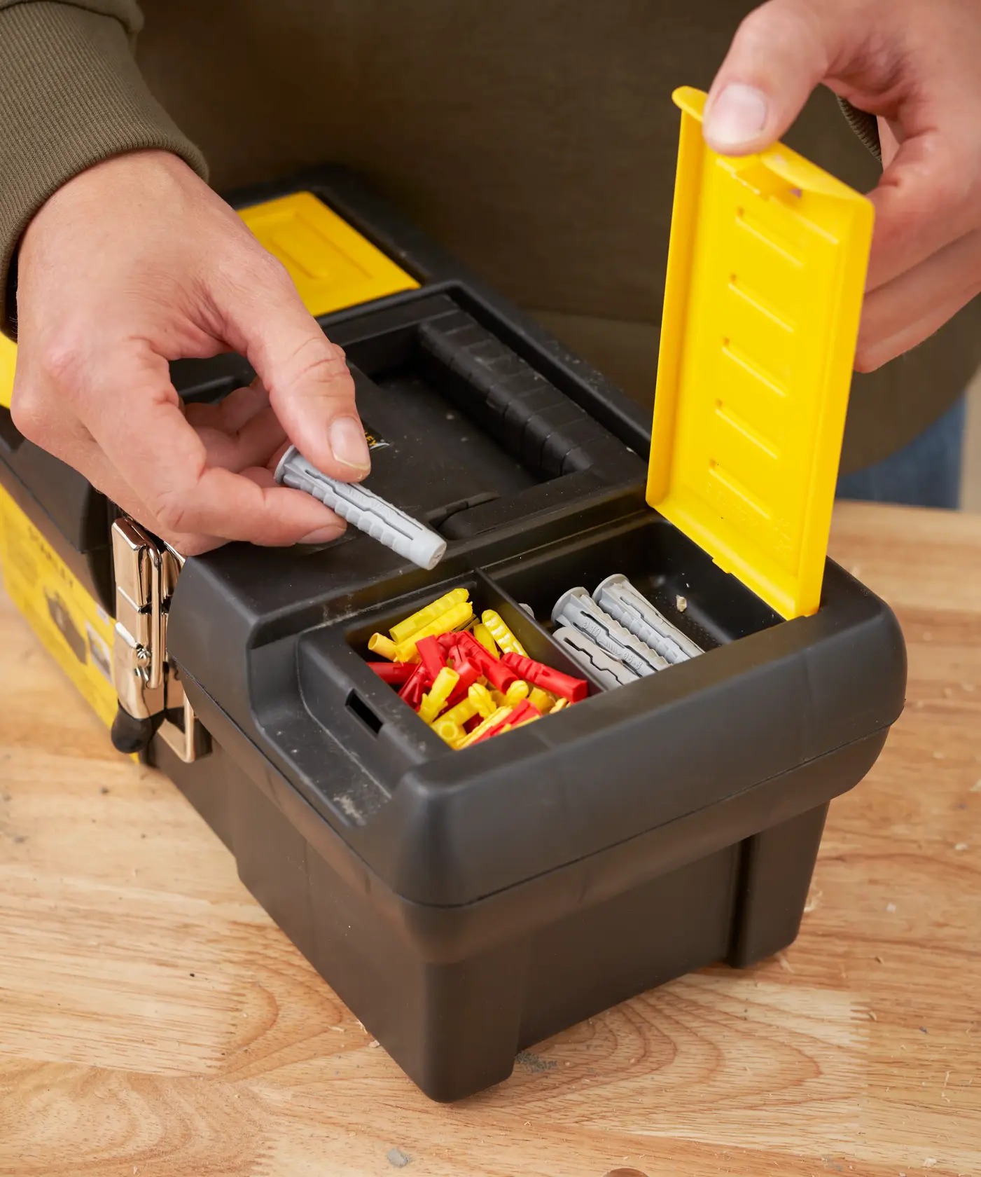 STANLEY 1-92-064 tool box with yellow lid, holding assorted wall plugs on a wood surface, close-up angle
