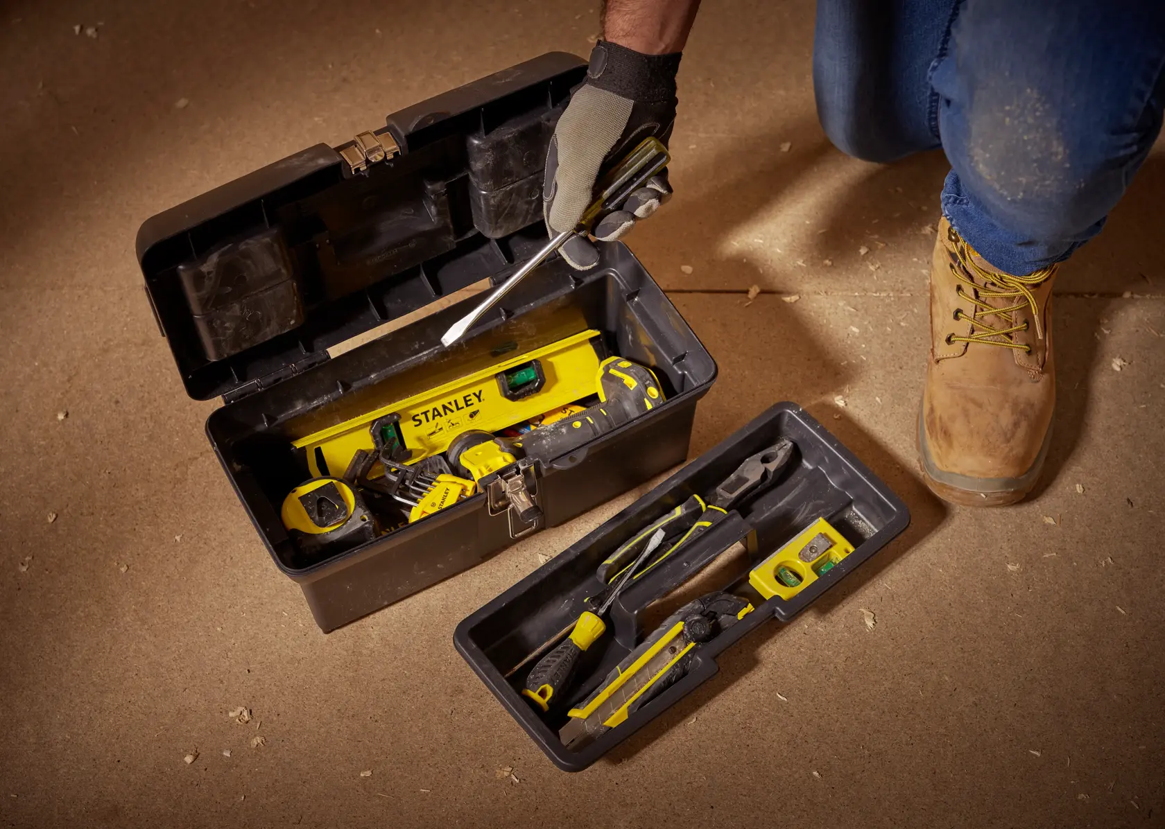 STANLEY 1-94-857 tool box opened with assorted hand tools and yellow level on indoor floor.