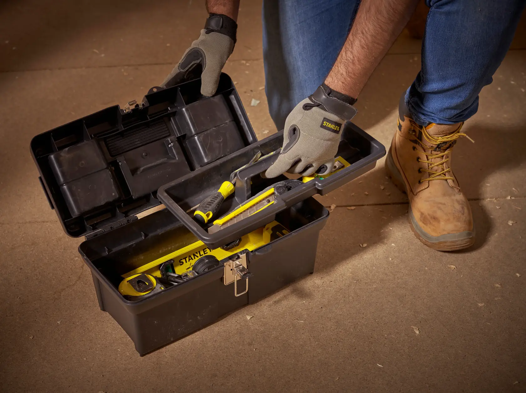 STANLEY 1-94-857 black toolbox opened with tools, person wearing gloves and boots holding tray.