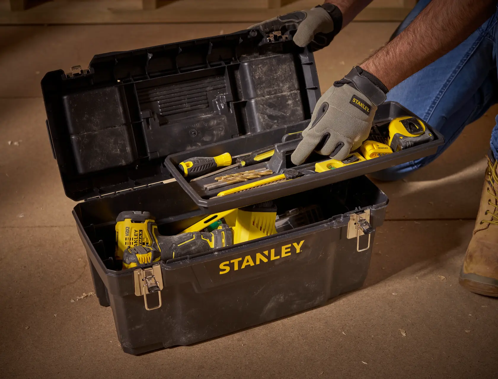 STANLEY 1-94-858 toolbox with yellow hand tools, open on floor, person wearing gloves lifts tray.