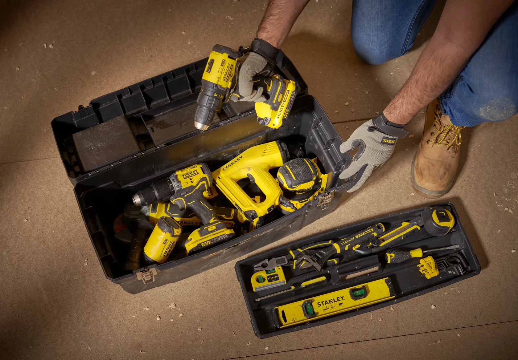 STANLEY 1-94-859 toolbox with yellow power tools and hand tools, top-down angle, on workshop floor.