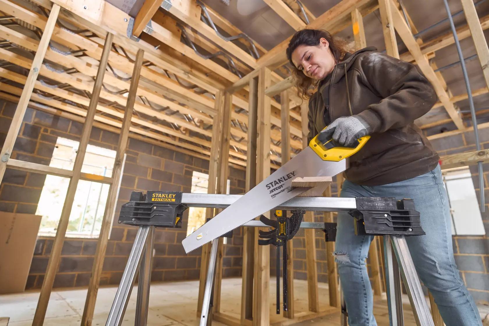 Photo of STANLEY 2-15-244 hand saw with yellow handle in use at a construction site, cutting wood on a sawhorse.