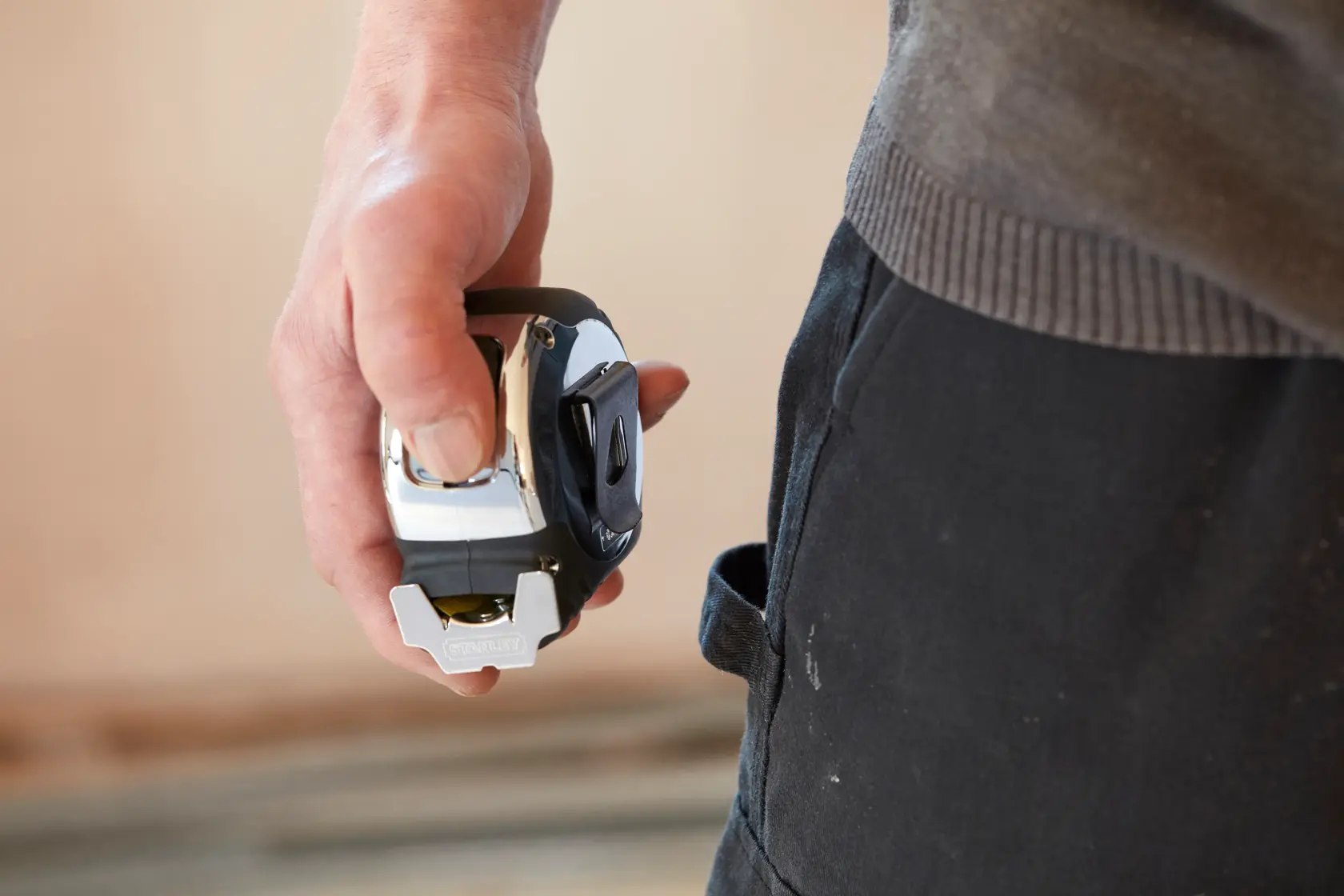 STANLEY 5-33-891 tape measure held in hand near work pants, product photography.