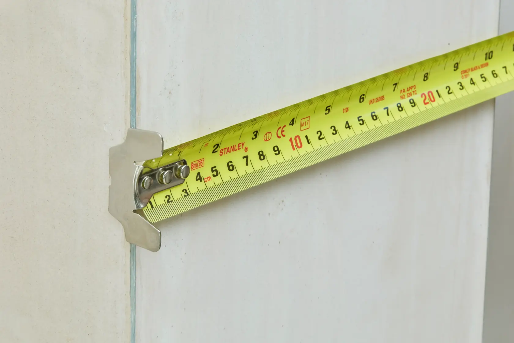 STANLEY 5-33-891 tape measure close-up with extended yellow blade, measuring against a light wall.