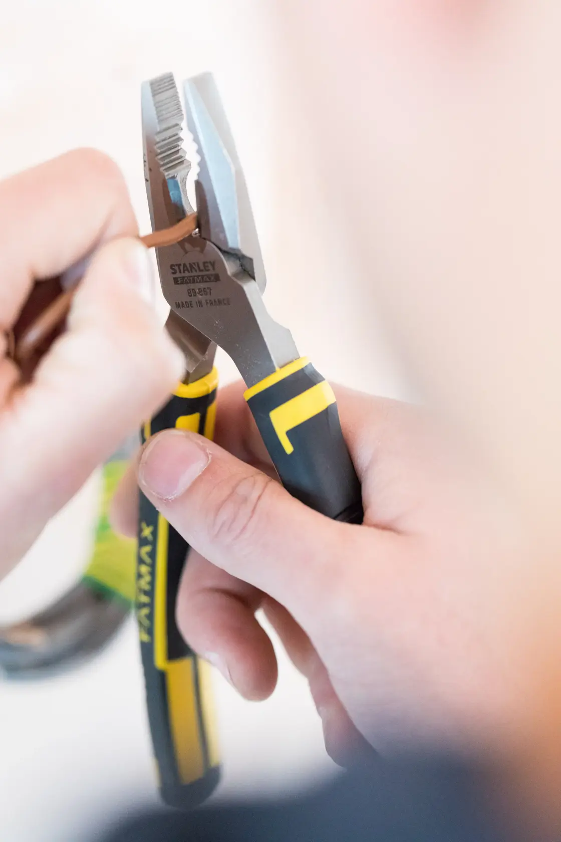 Photo of STANLEY 89-867 combination pliers with black and yellow handles gripping a brown wire in use.