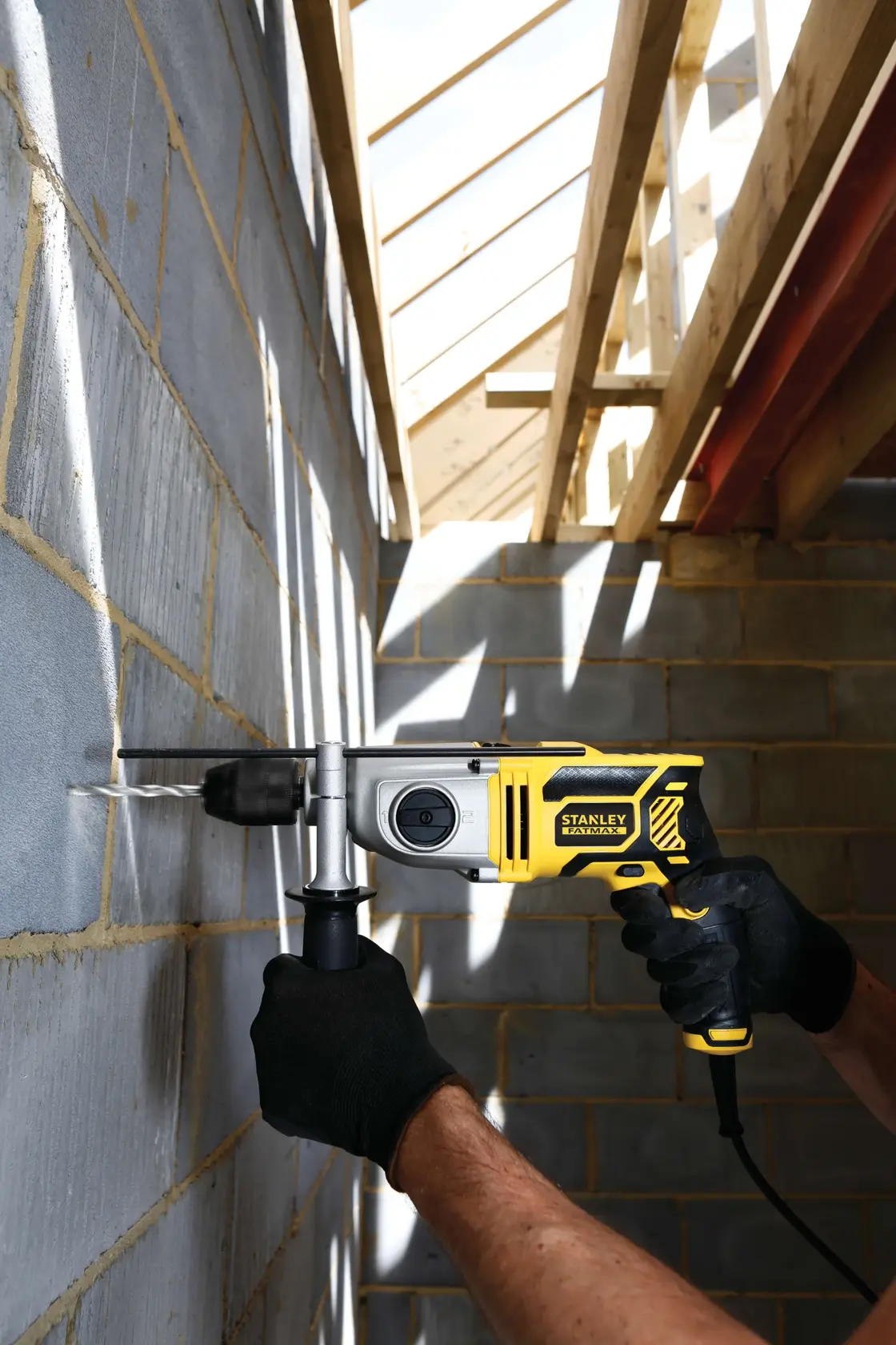 STANLEY FME142K corded hammer drill in use on masonry wall at construction site, shown from side angle.