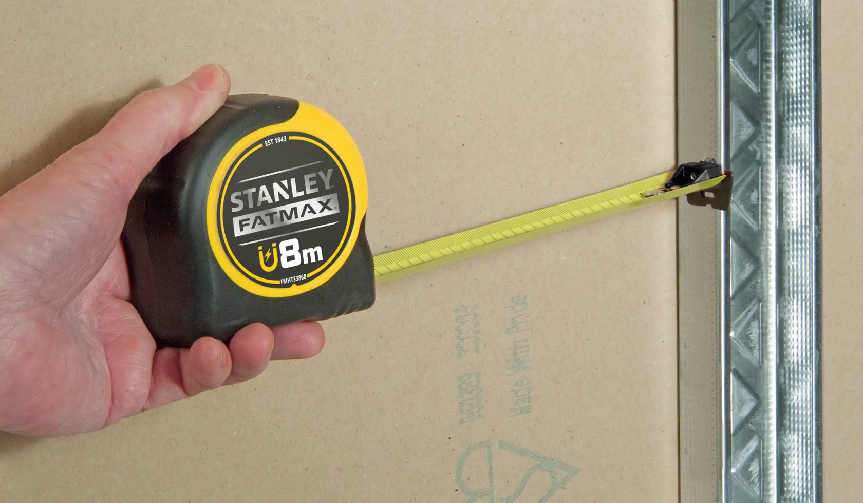 STANLEY FMHT0-33868 tape measure held in hand, yellow blade extended against drywall.