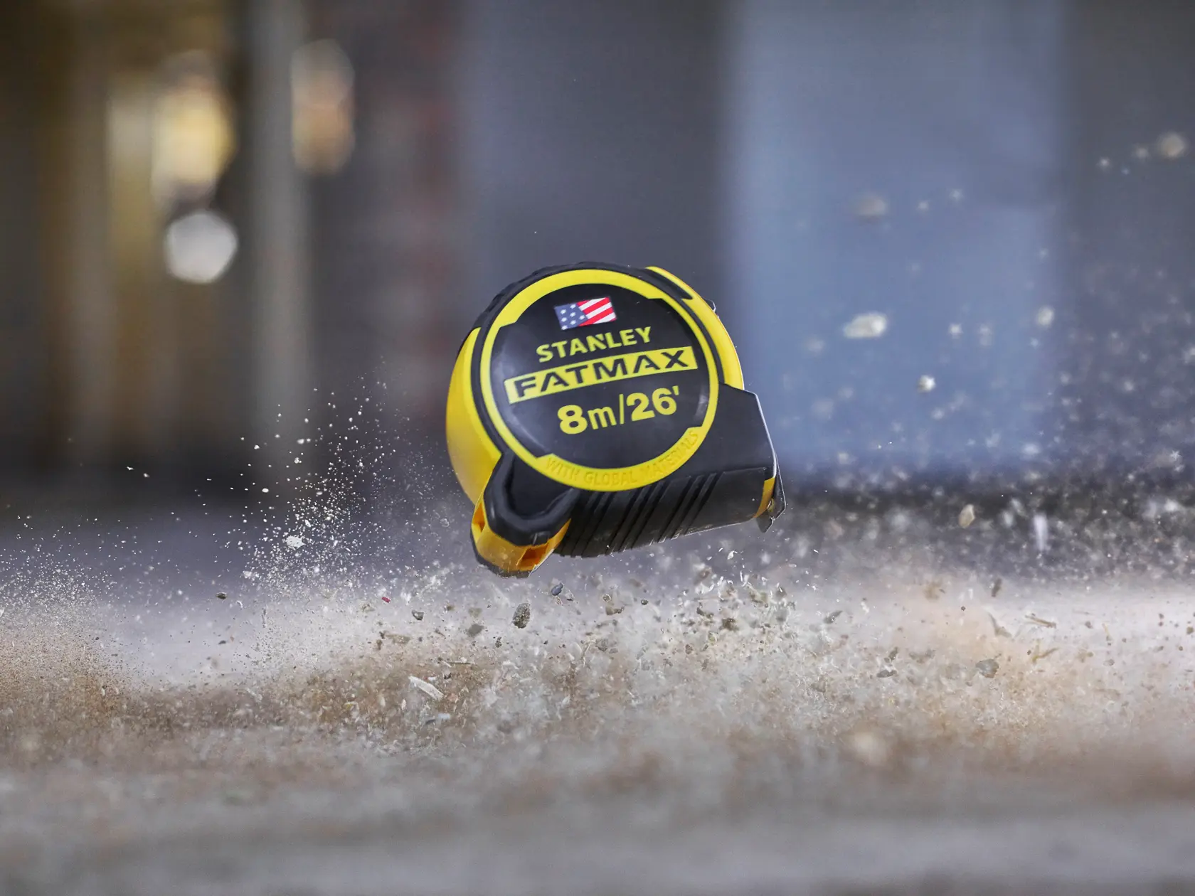 Stanley FMHT0-36326 FatMax tape measure 8m/26ft, yellow and black, in mid-air above dusty ground.