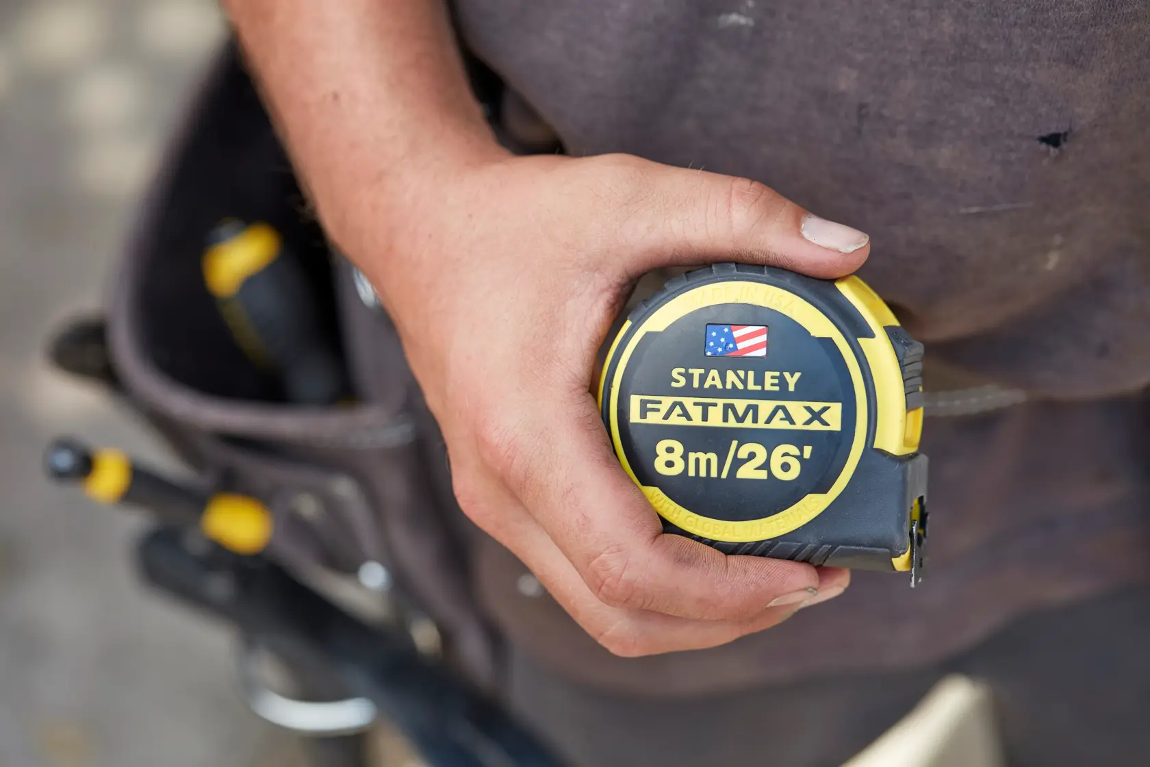 Photo of STANLEY FMHT0-36326 FATMAX tape measure, 8m/26', held in hand, tool belt in background.