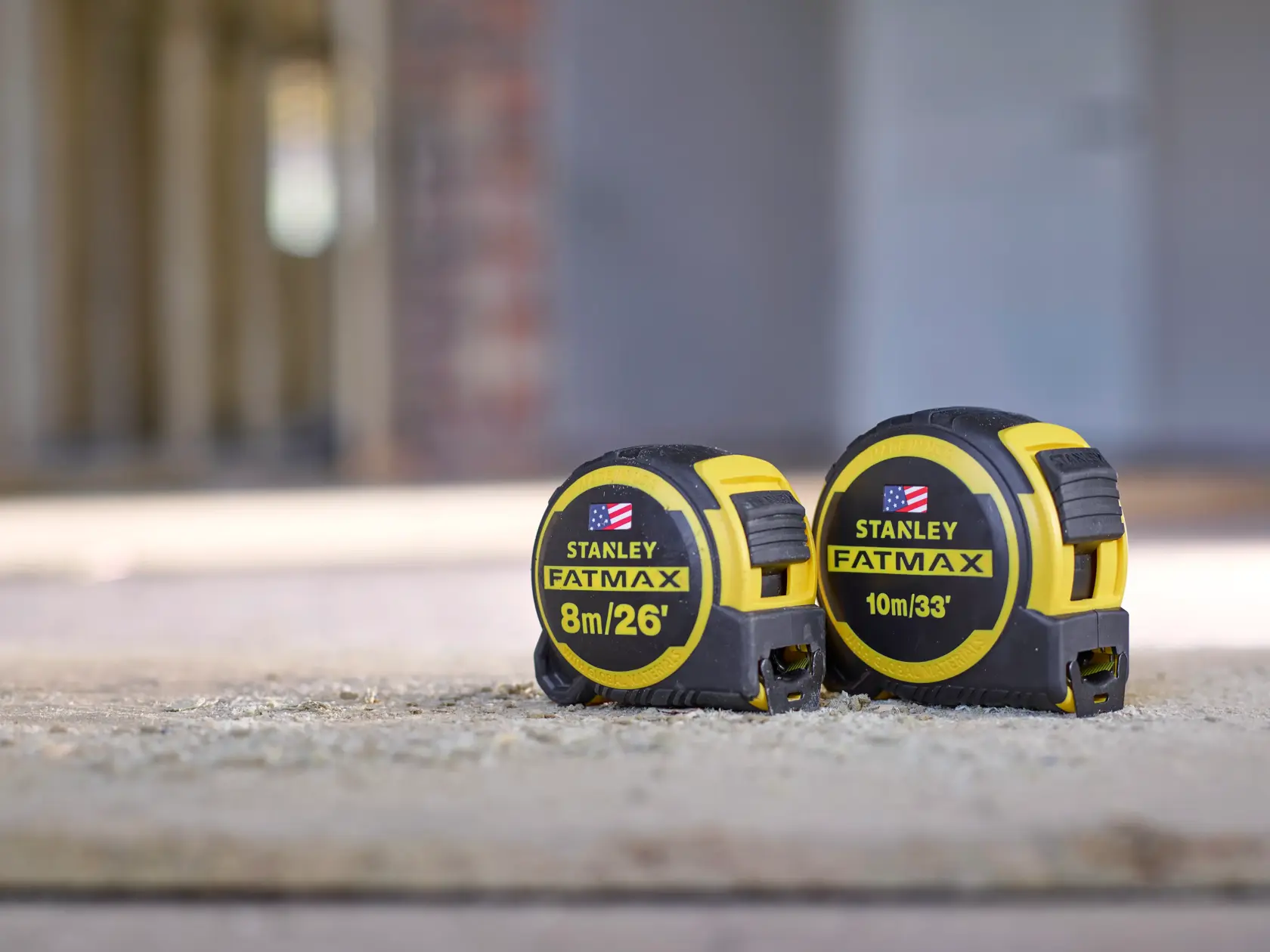 Photo of two STANLEY FMHT0-36336 FATMAX tape measures, 8m/26ft and 10m/33ft, on a construction surface.