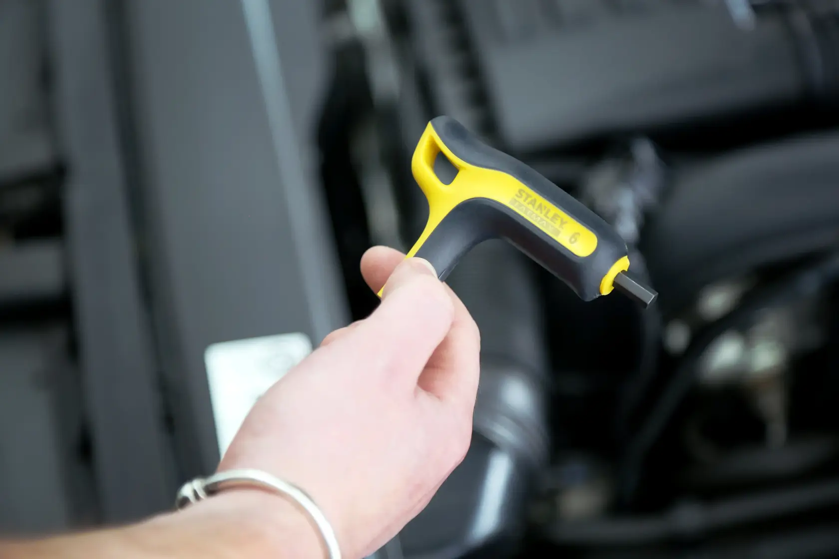 Stanley FMHT0-69049 hex key with yellow and black handle in hand near engine compartment.