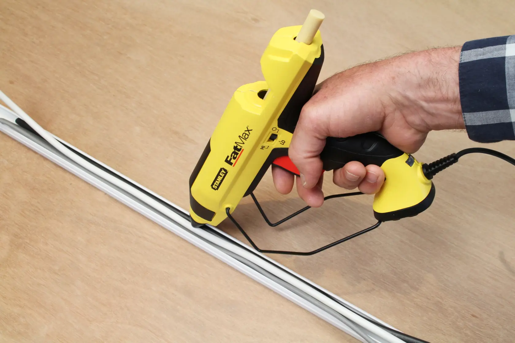 Photo of STANLEY FMHT0-70418 yellow FatMax glue gun applying adhesive to white strips on wood.