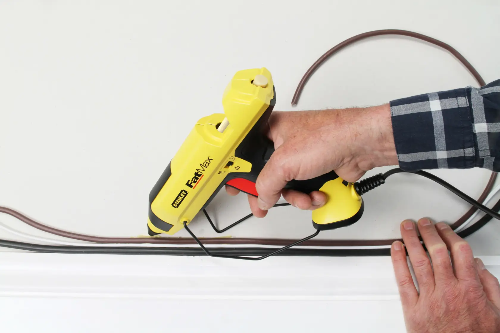 STANLEY FMHT0-70418 glue gun held against wall, applying adhesive to cables, close-up photo.