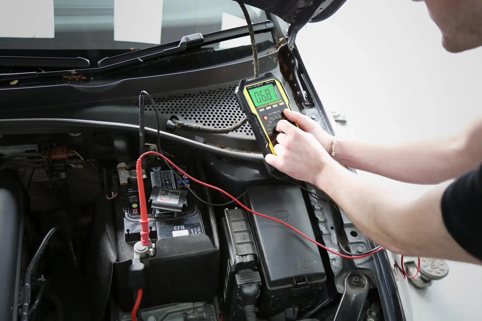 Photo of STANLEY FMHT0-77419 automotive multimeter testing a car battery, top view of engine compartment.