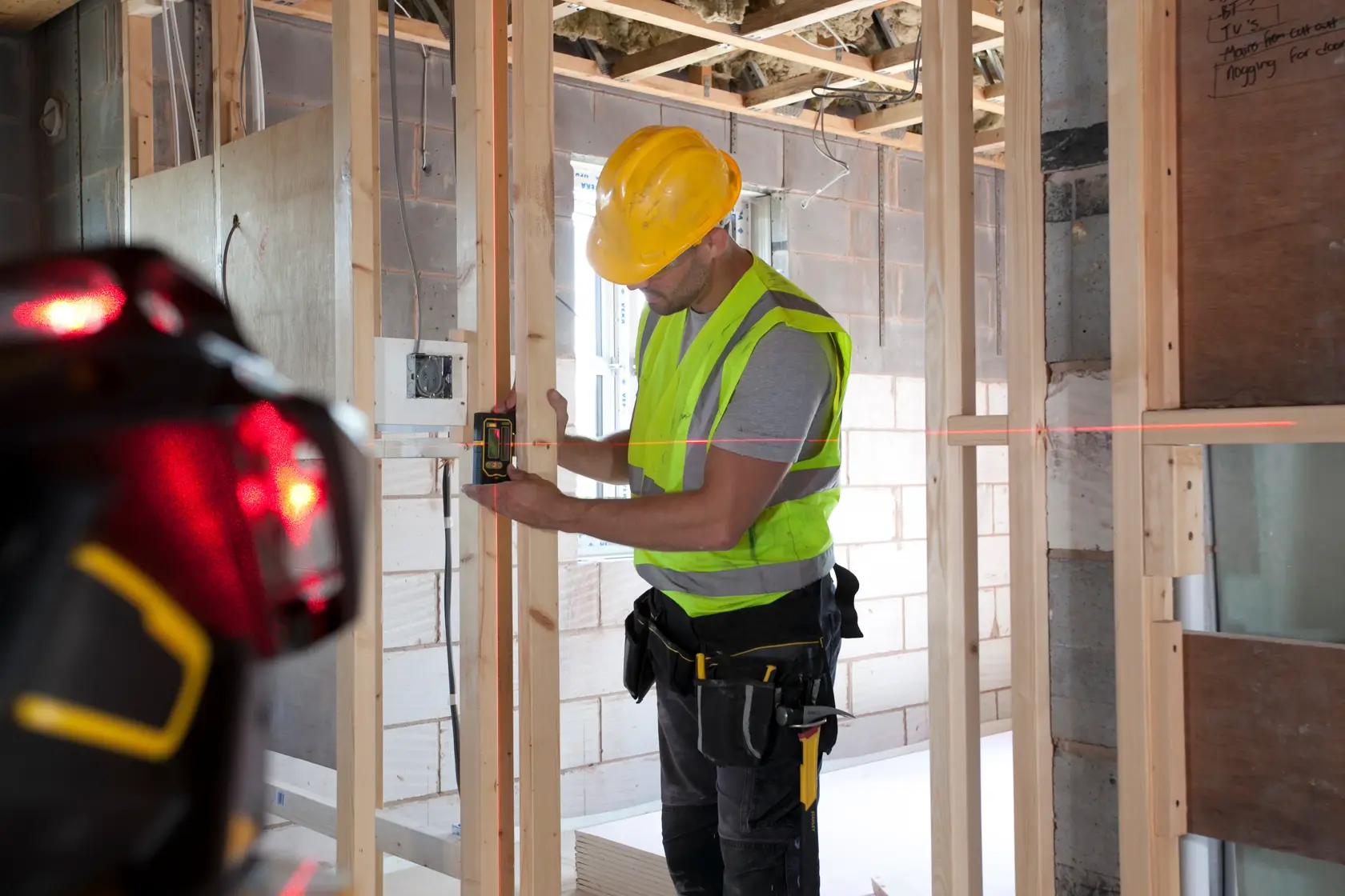 STANLEY FMHT1-77357 laser level used by worker in construction site, photography showing wall framing.