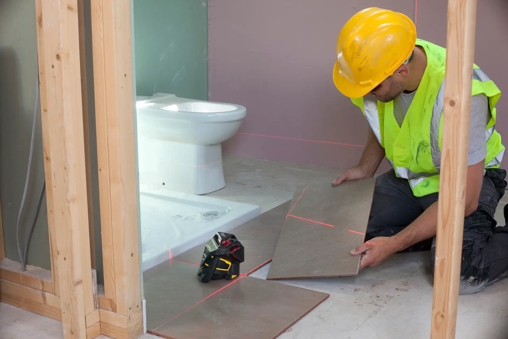 STANLEY FMHT1-77357 laser level used by worker aligning floor tiles in bathroom under construction.