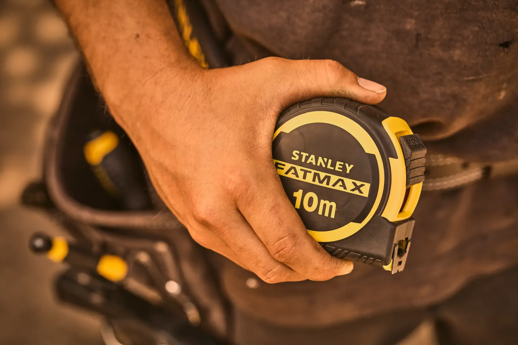 Photo of STANLEY FATMAX 10m tape measure FMHT33005-0 in hand, tool belt and tools in background.