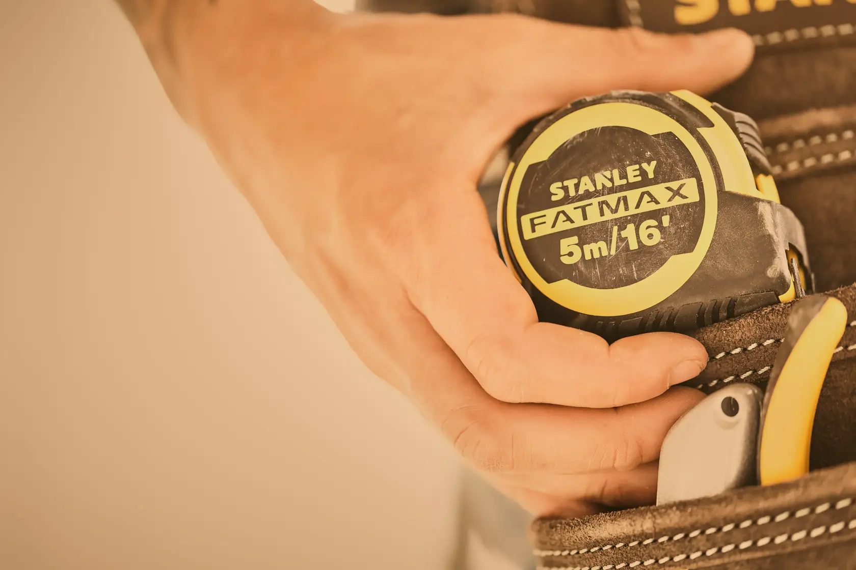 STANLEY FMHT33006-5 tape measure held by hand, yellow and black, close-up in tool belt.