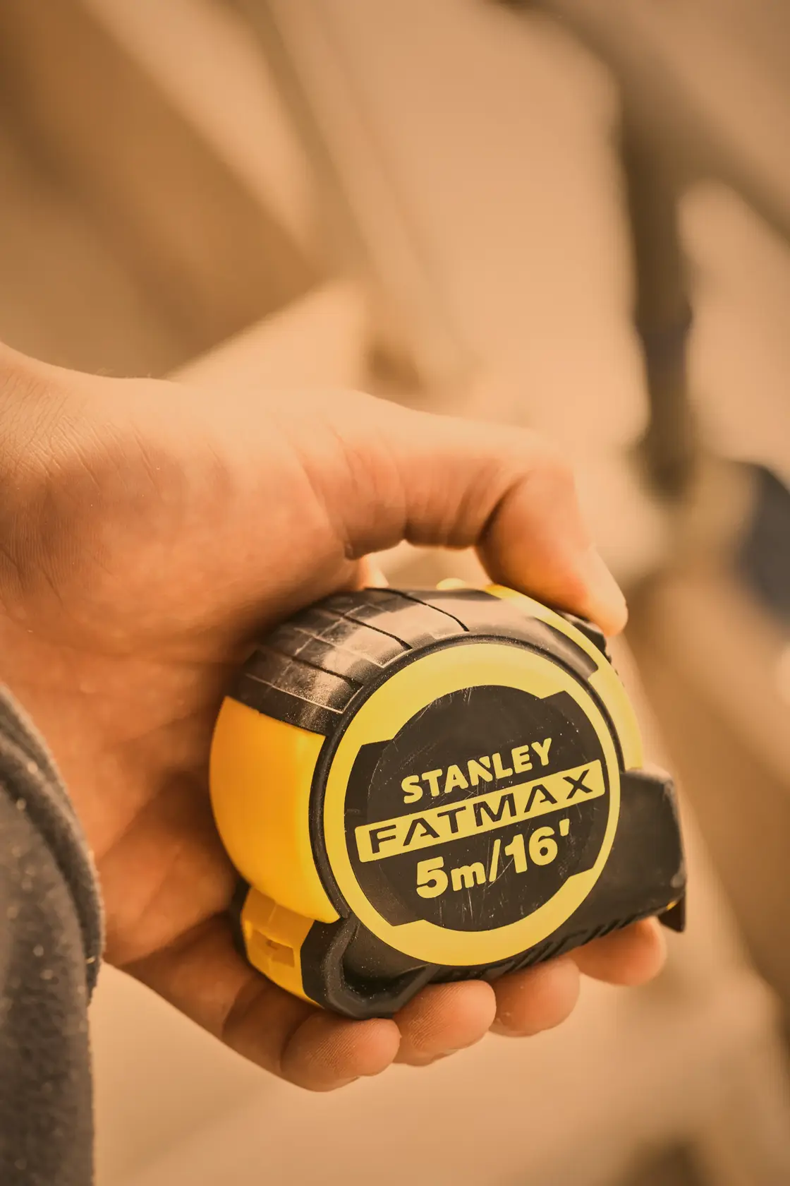 Photo of STANLEY FMHT33006-5 FatMax tape measure, yellow and black, held in hand, product close-up.