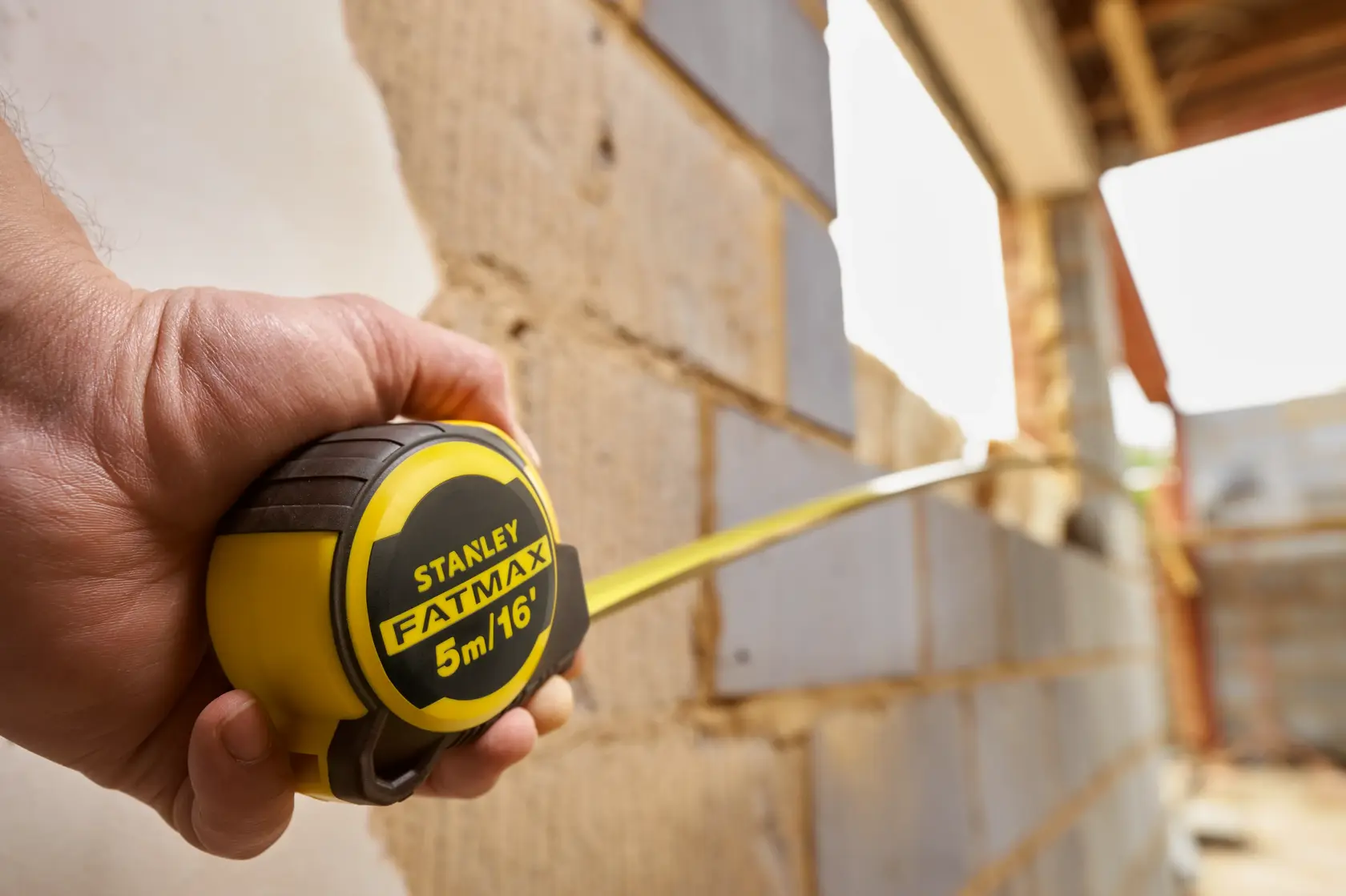 STANLEY FMHT33006-5 tape measure held, yellow and black, measuring wall, FATMAX logo visible.