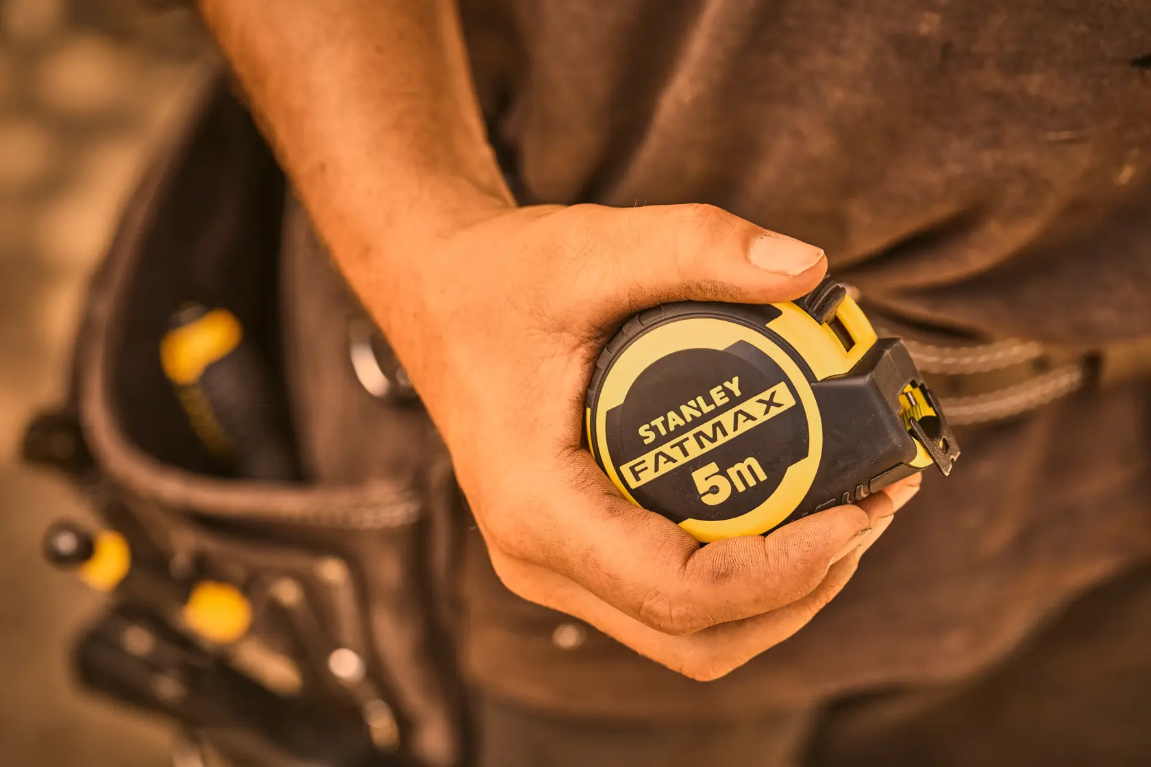 Photo of STANLEY FMHT33100-0 FATMAX 5m tape measure held in hand, tool belt in background.