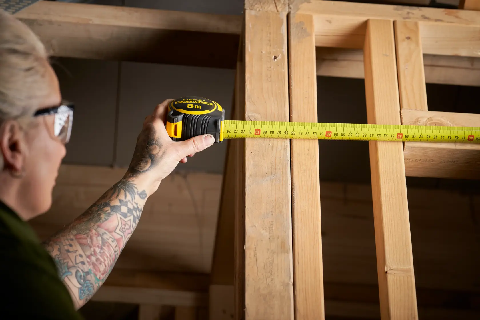 STANLEY FMHT33102-0 tape measure in use measuring wooden frame, side view, yellow and black casing visible.