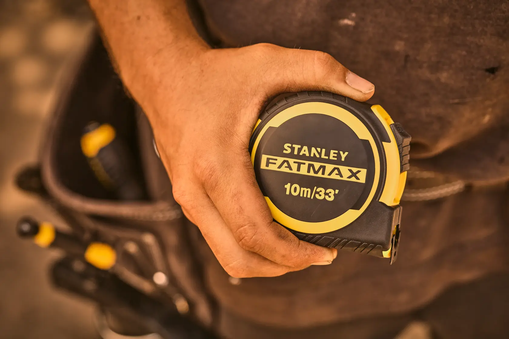 Photo of STANLEY FATMAX FMHT33104-5 tape measure 10m/33', yellow and black, held in a worker's hand.