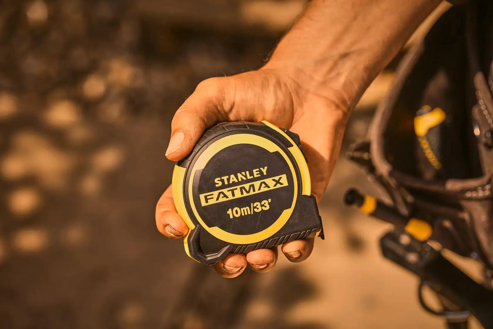 Photo of STANLEY FATMAX 10m/33' tape measure FMHT33104-5 in a worker's hand outdoors.