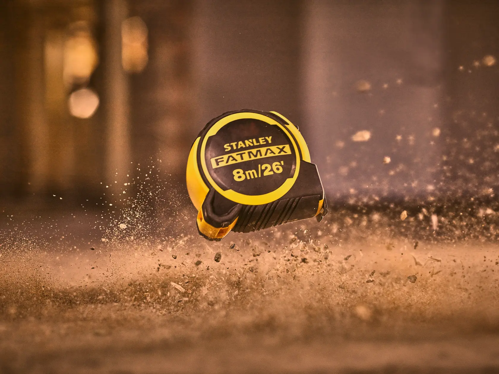 Photography of STANLEY FATMAX 8m/26' tape measure SKU FMHT33105-5, yellow and black, in mid-air with dust.