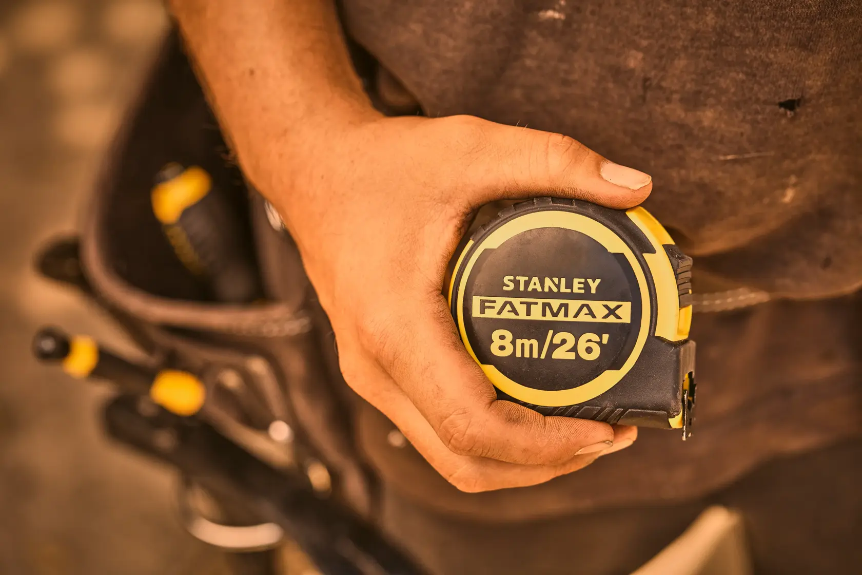 STANLEY FATMAX 8m/26' tape measure FMHT33105-5 held in hand, tool belt visible in background.