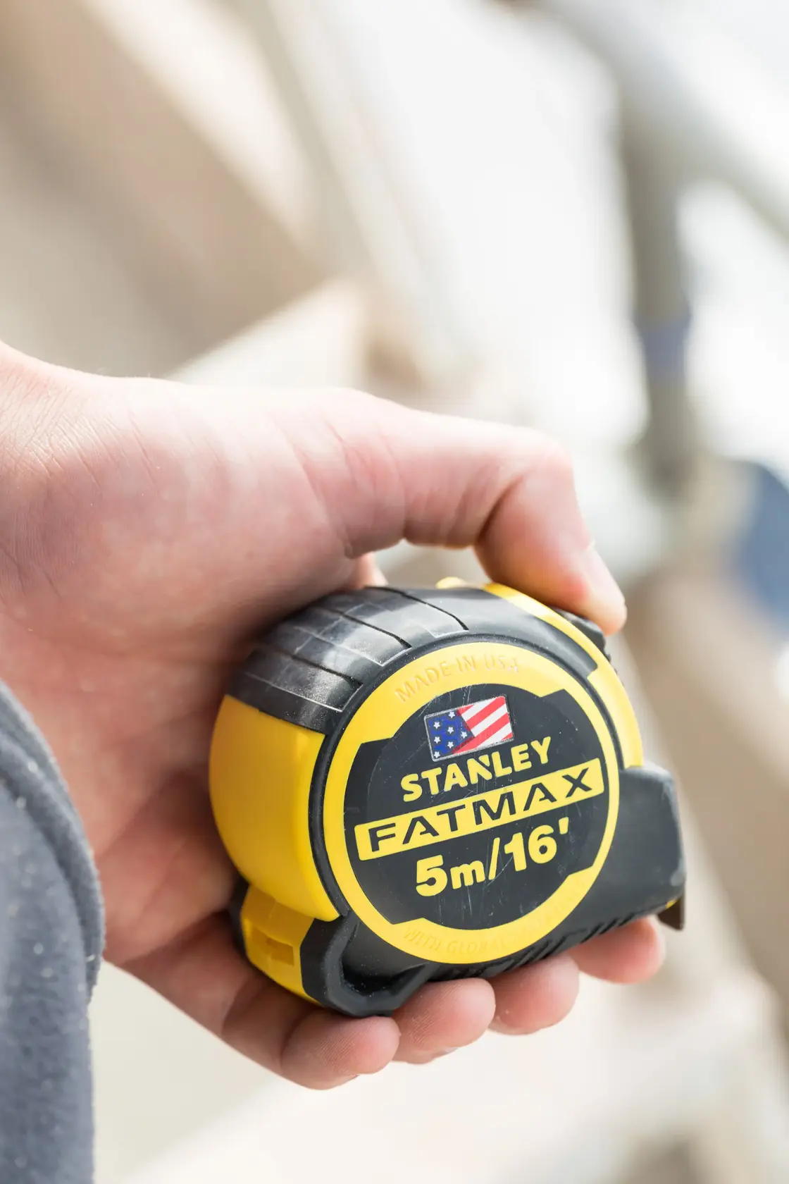 Photo of STANLEY FMHT36317-0 FATMAX tape measure, 5m/16ft, in hand, yellow and black casing.