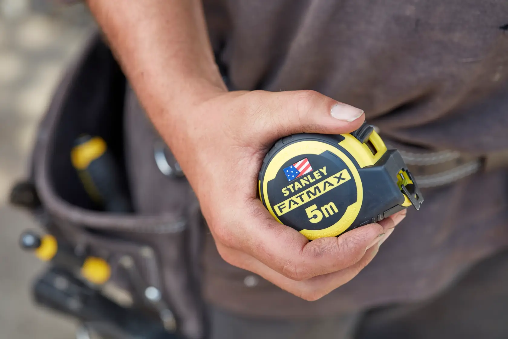 Photo of STANLEY FMHT36318-0 FATMAX 5m tape measure held in hand with tool belt in background.