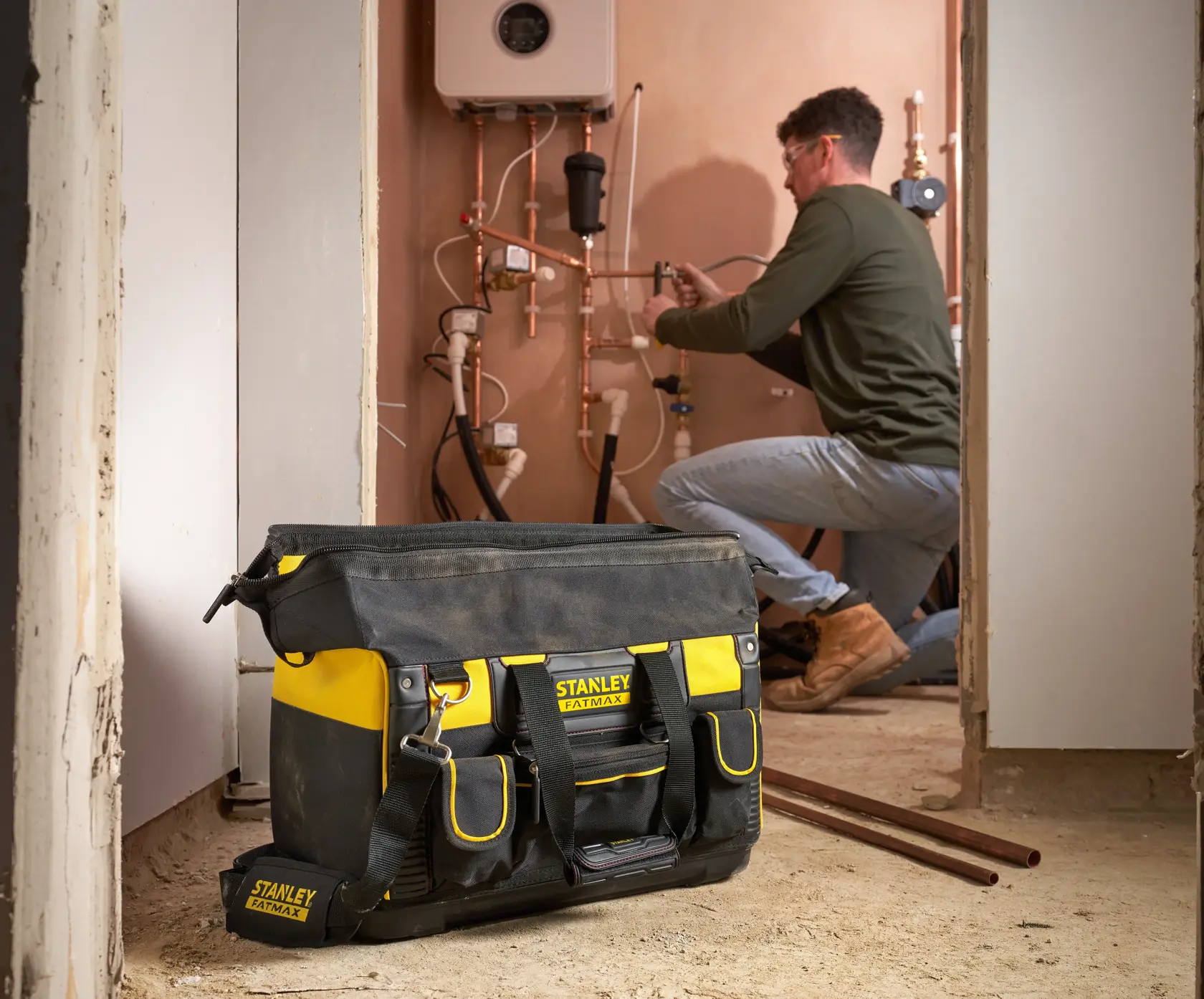 STANLEY FMST1-71180 tool bag in black and yellow with external pockets, shown on a construction site floor.